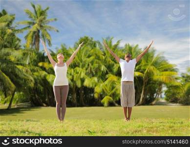 fitness, sport and people concept - happy couple making yoga and meditating over exotic natural background with palm trees. happy couple making yoga exercises on beach