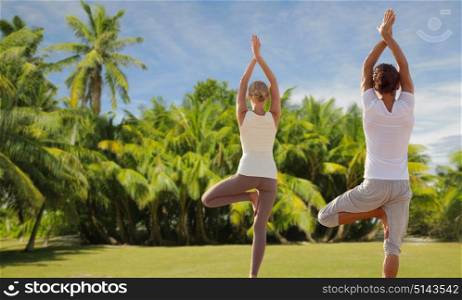 fitness, sport and people concept - happy couple making yoga and meditating over exotic natural background with palm trees. happy couple making yoga exercises on beach