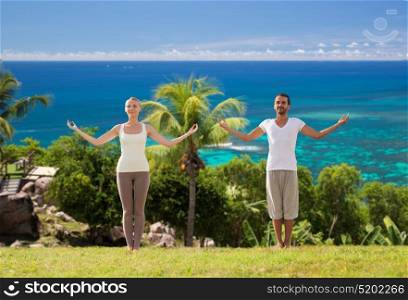 fitness, sport and people concept - happy couple making yoga and meditating over natural background. happy couple making yoga exercises on beach