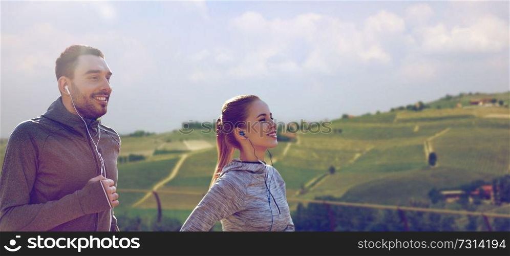 fitness, sport and people concept - happy couple running and listening to music in earphones over country landscape background. happy couple with earphones running outdoors