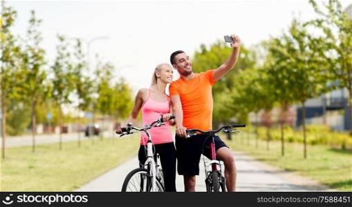 fitness, sport and people concept - happy couple with bicycles taking selfie by smartphone over city street on background. couple with bicycles taking selfie by smartphone