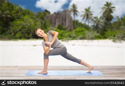 fitness, sport and people concept - happy smiling woman doing yoga side angle pose on mat over exotic tropical beach background. woman doing yoga side angle pose on beach