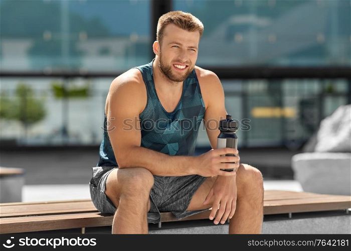 fitness, sport and people concept - happy smiling young man with bottle of water sitting on city bench. happy sportsman with bottle sitting on city bench