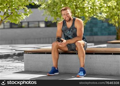 fitness, sport and people concept - happy smiling young man with bottle of water sitting on city bench. happy sportsman with bottle sitting on city bench