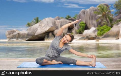 fitness, sport and people concept - happy woman doing yoga and stretching on mat over exotic tropical beach background. happy woman doing yoga and stretching on beach