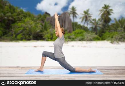 fitness, sport and people concept - happy woman doing yoga in low lunge pose on mat over exotic tropical beach background. happy woman doing yoga in low lunge on beach