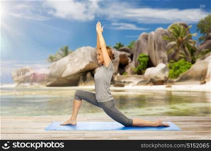 fitness, sport and people concept - happy woman doing yoga in low lunge pose on mat over exotic tropical beach background. happy woman doing yoga in low lunge on beach