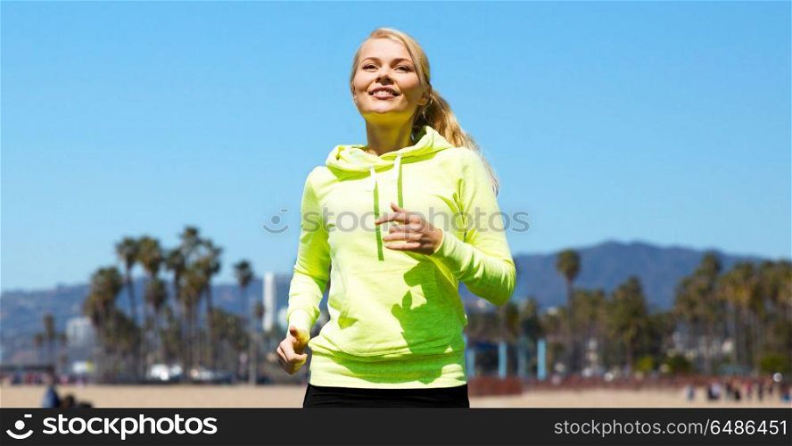 fitness, sport and people concept - happy woman running over venice beach background in california. woman running over venice beach. woman running over venice beach