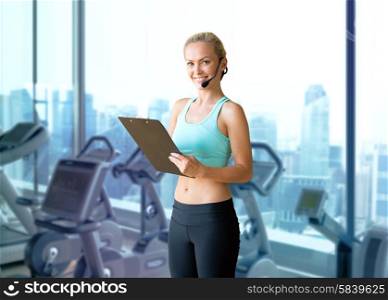 fitness, sport and people concept - happy woman sports trainer with microphone and clipboard over gym machines background