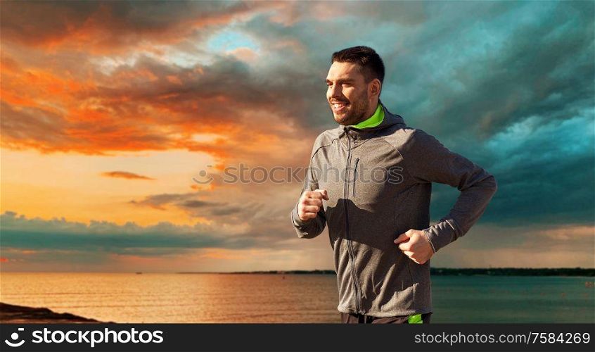 fitness, sport and people concept - happy young man running over sea and sunset sky on background. happy young man running over sea and sunset sky