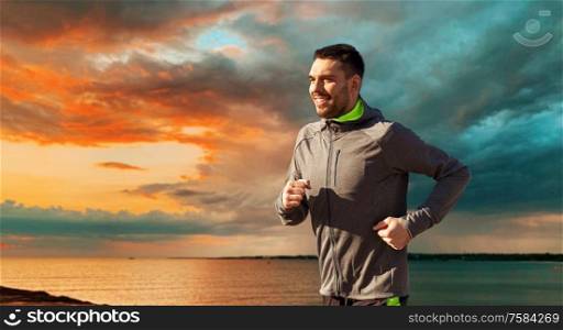 fitness, sport and people concept - happy young man running over sea and sunset sky on background. happy young man running over sea and sunset sky