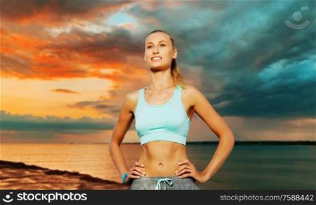 fitness, sport and people concept - happy young woman exercising over sea and sunset sky on background. happy young woman exercising over sea