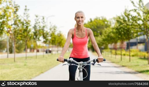 fitness, sport and people concept - happy young woman riding bicycle along road on city street background. happy young woman riding bicycle outdoors