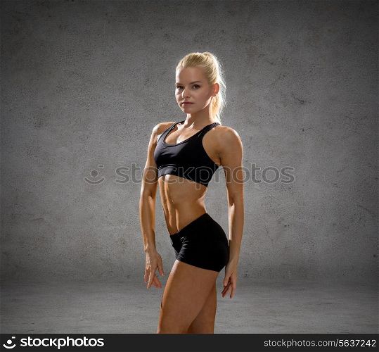 fitness, sport and people concept - smiling athletic woman in sportswear over concrete wall background