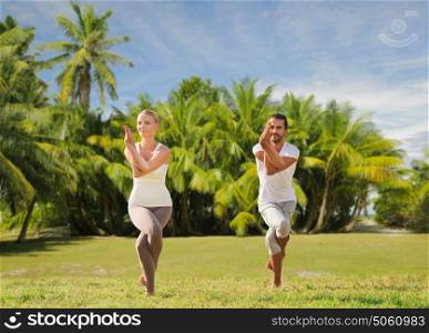 fitness, sport and people concept - smiling couple making yoga in eagle pose outdoors over exotic natural background with palm trees. smiling couple making yoga exercises outdoors