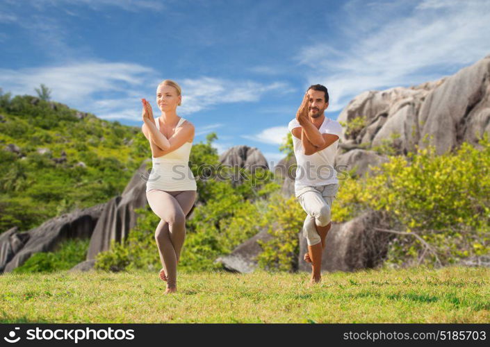 fitness, sport and people concept - smiling couple making yoga in eagle pose outdoors over natural background. smiling couple making yoga exercises outdoors