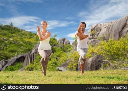fitness, sport and people concept - smiling couple making yoga in eagle pose outdoors over natural background. smiling couple making yoga exercises outdoors