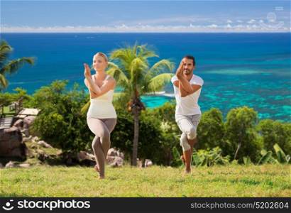 fitness, sport and people concept - smiling couple making yoga in eagle pose outdoors over natural background. smiling couple making yoga exercises outdoors