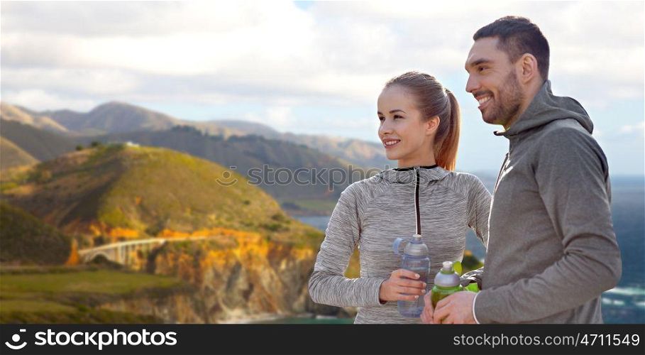 fitness, sport and people concept - smiling couple with bottles of water over bixby creek bridge on big sur coast of california background. couple of sportsmen with water over big sur coast. couple of sportsmen with water over big sur coast
