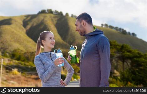 fitness, sport and people concept - smiling couple with bottles of water over big sur hills background in california. couple of sportsmen with water over big sur hills. couple of sportsmen with water over big sur hills