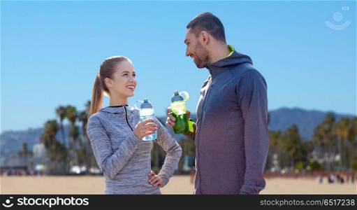 fitness, sport and people concept - smiling couple with bottles of water over venice beach background in california. couple of sportsmen with water over venice beach. couple of sportsmen with water over venice beach