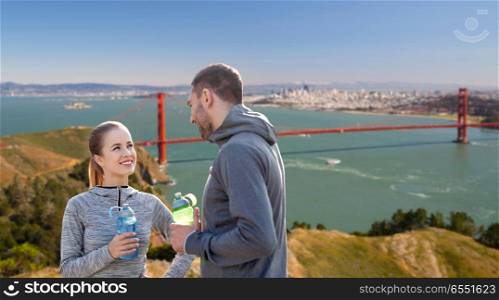 fitness, sport and people concept - smiling couple with bottles of water over golden gate bridge in san francisco bay background. couple of sportsmen with water over san francisco. couple of sportsmen with water over san francisco