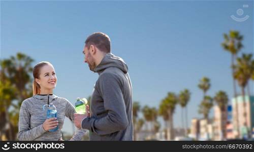 fitness, sport and people concept - smiling couple with bottles of water over venice beach background in california. couple of sportsmen with water over venice beach. couple of sportsmen with water over venice beach