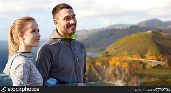 fitness, sport and people concept - smiling couple with bottles of water over bixby creek bridge on big sur coast of california background. couple of sportsmen with water over big sur coast