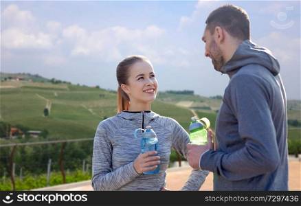 fitness, sport and people concept - smiling couple with bottles of water over country landscape background. couple with bottles of water after sports outdoors