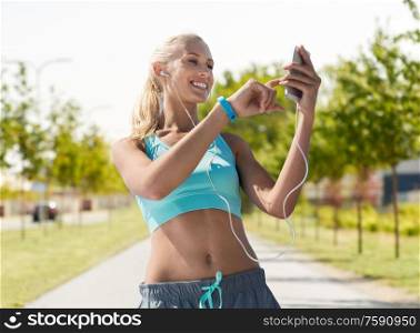 fitness, sport and people concept - smiling young woman with smartphone and earphones listening to music and exercising over city street on background. happy woman with smartphone and earphones outdoors