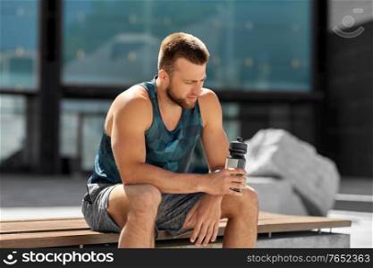 fitness, sport and people concept - tired young man with bottle of water sitting on city bench. tired sportsman with bottle sitting on city bench