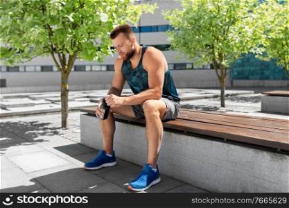 fitness, sport and people concept - tired young man with bottle of water sitting on city bench. tired sportsman with bottle sitting on city bench