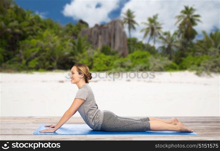 fitness, sport and people concept - woman doing yoga in dog pose on mat over exotic tropical beach background. woman doing yoga in dog pose on beach