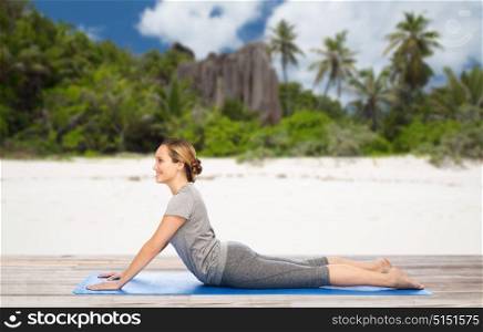 fitness, sport and people concept - woman doing yoga in dog pose on mat over exotic tropical beach background. woman doing yoga in dog pose on beach