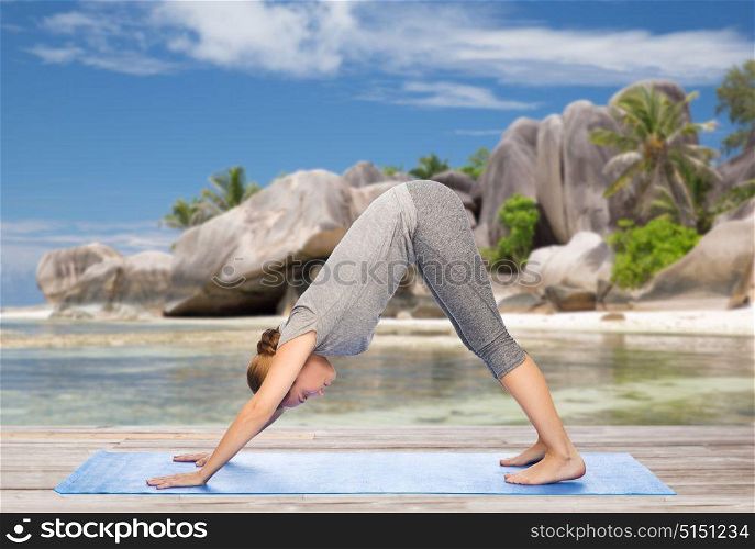 fitness, sport and people concept - woman doing yoga in downward facing dog pose on mat over exotic tropical beach background. woman doing yoga dog pose on beach