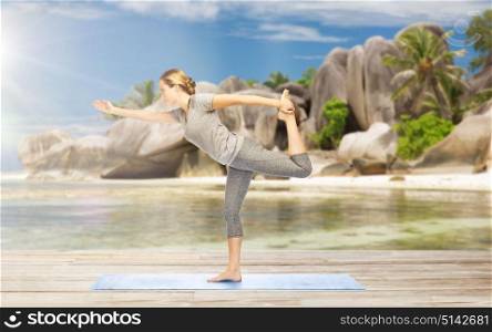 fitness, sport and people concept - woman doing yoga in lord of the dance pose on mat over exotic tropical beach background. woman in yoga lord of the dance pose on beach