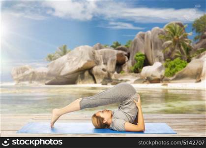fitness, sport and people concept - woman doing yoga in plow pose on mat over exotic tropical beach background. woman doing yoga in plow pose on beach
