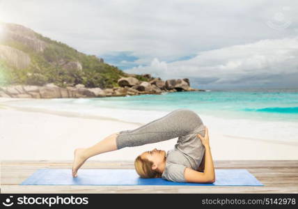 fitness, sport and people concept - woman doing yoga in plow pose on mat over exotic tropical beach background. woman doing yoga in plow pose on beach