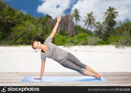 fitness, sport and people concept - woman doing yoga in side plank pose on mat over exotic tropical beach background. woman doing yoga in side plank pose on beach