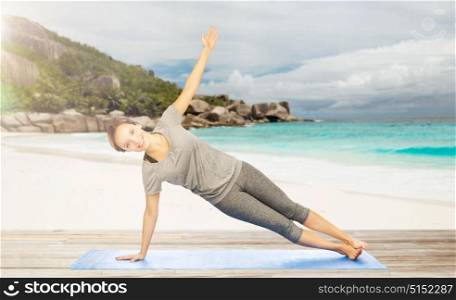 fitness, sport and people concept - woman doing yoga in side plank pose on mat over exotic tropical beach background. woman doing yoga in side plank pose on beach