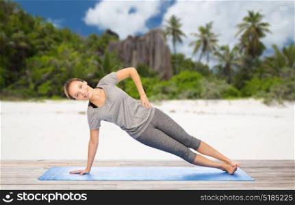 fitness, sport and people concept - woman doing yoga in side plank pose on mat over exotic tropical beach background. woman doing yoga in side plank pose on beach