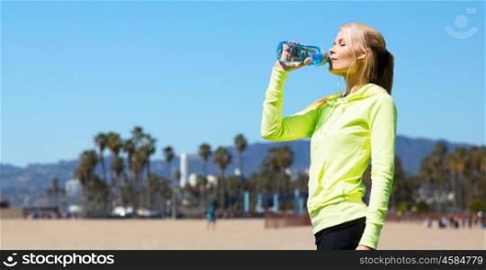 fitness, sport and people concept - woman drinking water after training over venice beach background in california. woman drinking water after doing sports outdoors. woman drinking water after doing sports outdoors