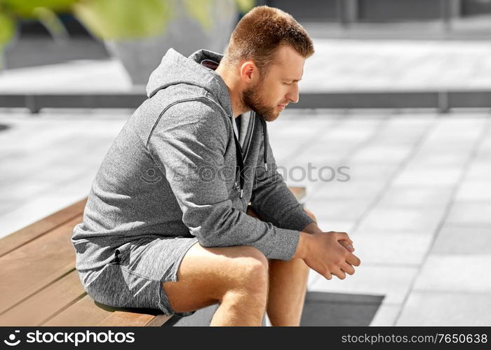 fitness, sport and people concept - young man sitting on bench outdoors. young man sitting on bench outdoors