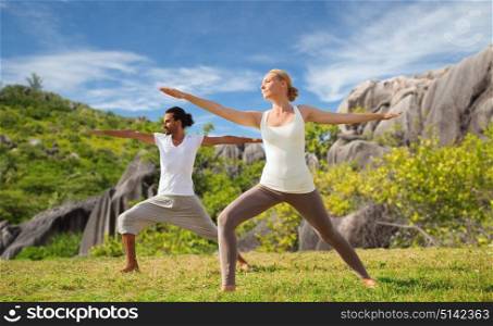 fitness, sport and relax concept - couple making yoga in warrior pose over natural background. couple making yoga in warrior pose at seaside
