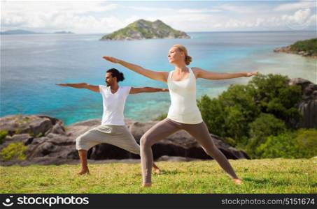 fitness, sport and relax concept - couple making yoga in warrior pose over natural background. couple making yoga in warrior pose at seaside
