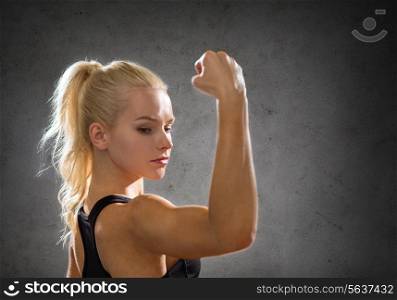 fitness, sport and strength concept - sporty woman flexing her biceps over concrete wall background