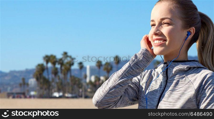 fitness, sport and technology concept - close up of happy woman listening to music in earphones over venice beach background in california. close up of woman listening to music in earphones. close up of woman listening to music in earphones