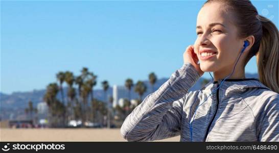 fitness, sport and technology concept - close up of happy woman listening to music in earphones over venice beach background in california. close up of woman listening to music in earphones. close up of woman listening to music in earphones