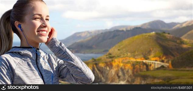 fitness, sport and technology concept - close up of happy woman listening to music in earphones over bixby creek bridge on big sur coast of california background. close up of woman listening to music in earphones. close up of woman listening to music in earphones