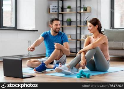 fitness, sport and technology concept - happy couple with laptop computer doing sports at home. happy couple with laptop doing sports at home